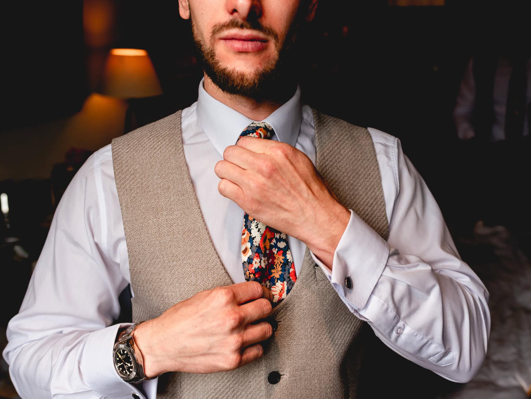 Groom fixes his flowery tie wearing beige waistcoat