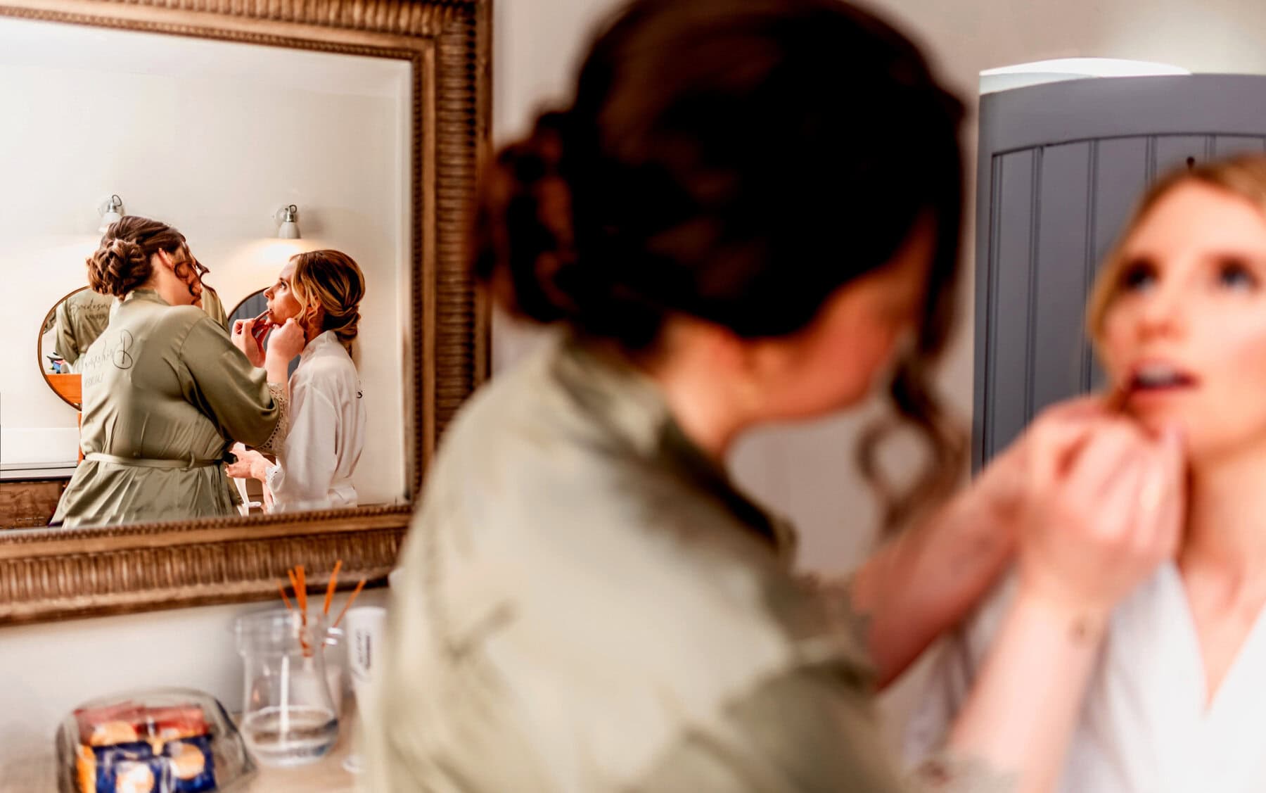 Bride has her make up applied, seen in the reflection of the mirror