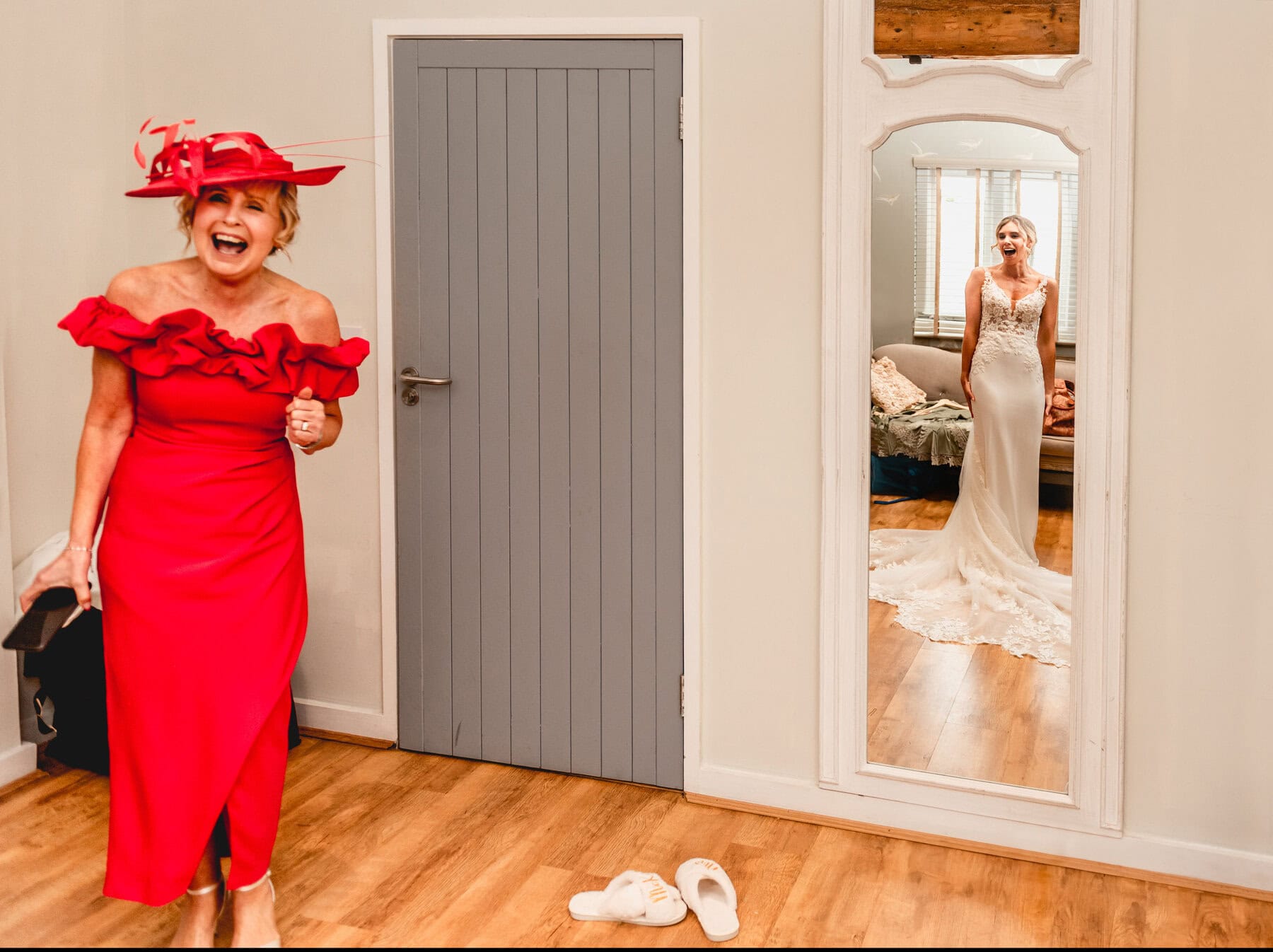Brides Mom wearing red dress sees her daughter as a bride for the first time. Bride is shown in reflection