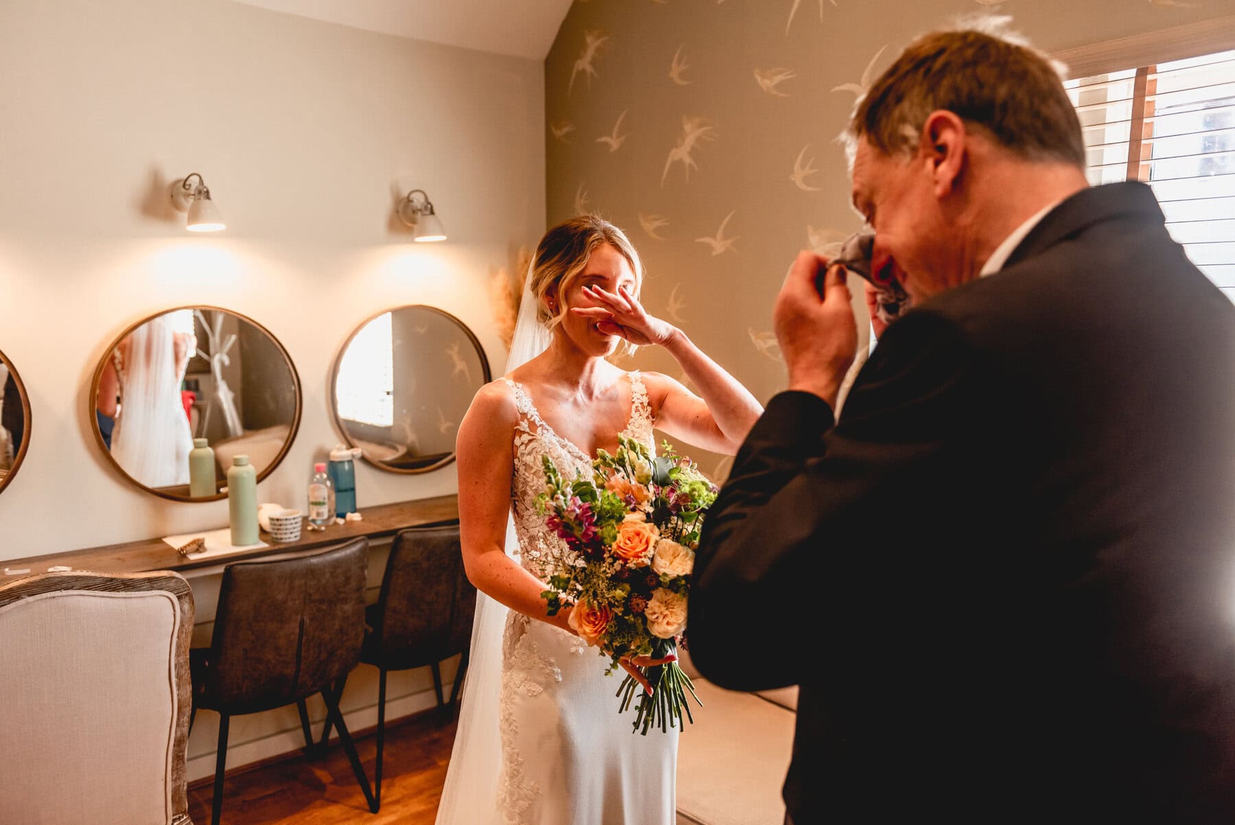 Bride and father cry as they see each other for the first time before the ceremony at Swallows Nest Barn. Both cry and wipe the tears from their eyes