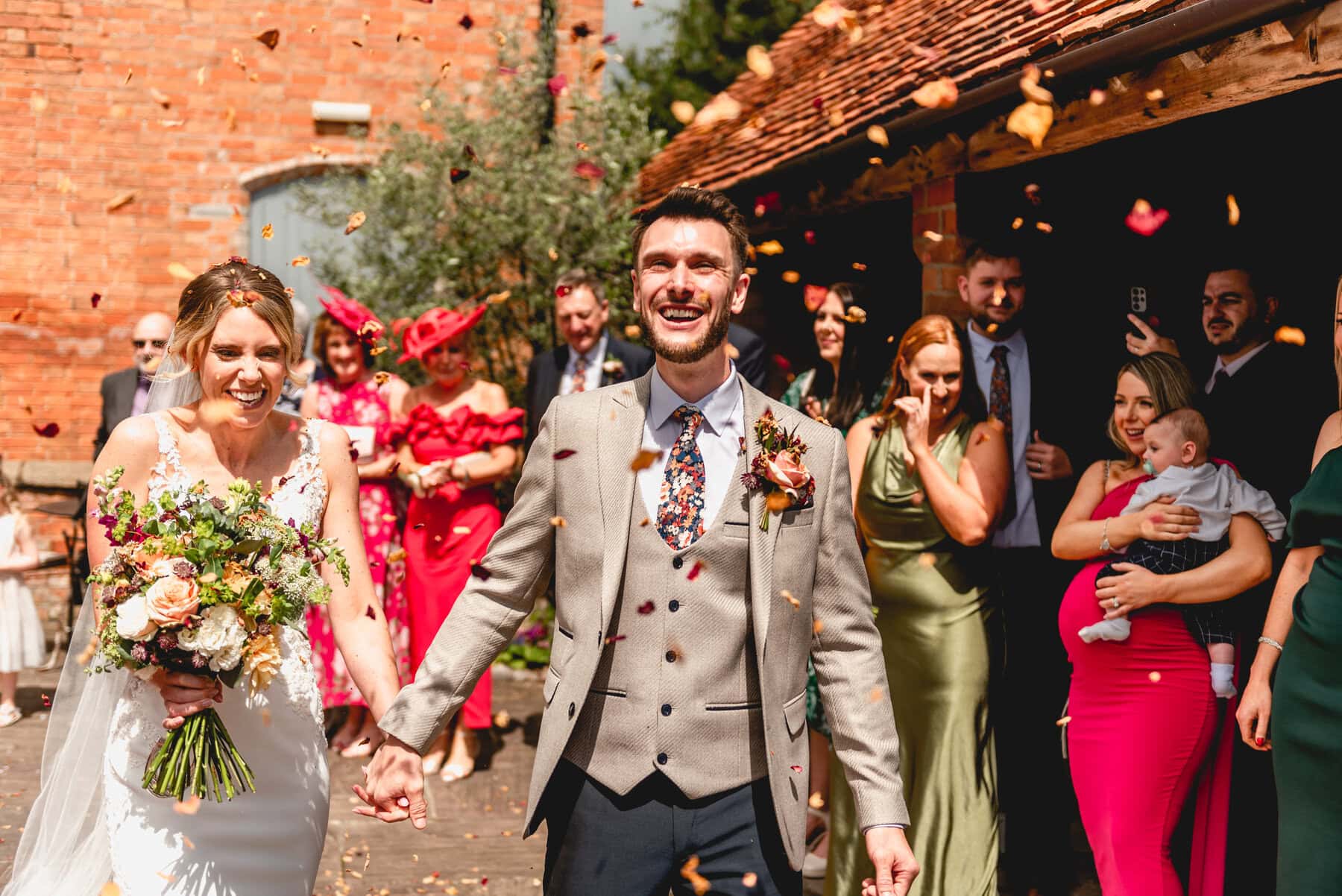 Confetti tunnel at Swallows Nest Barn, bride and groom hold hands and laugh as confetti lands on them