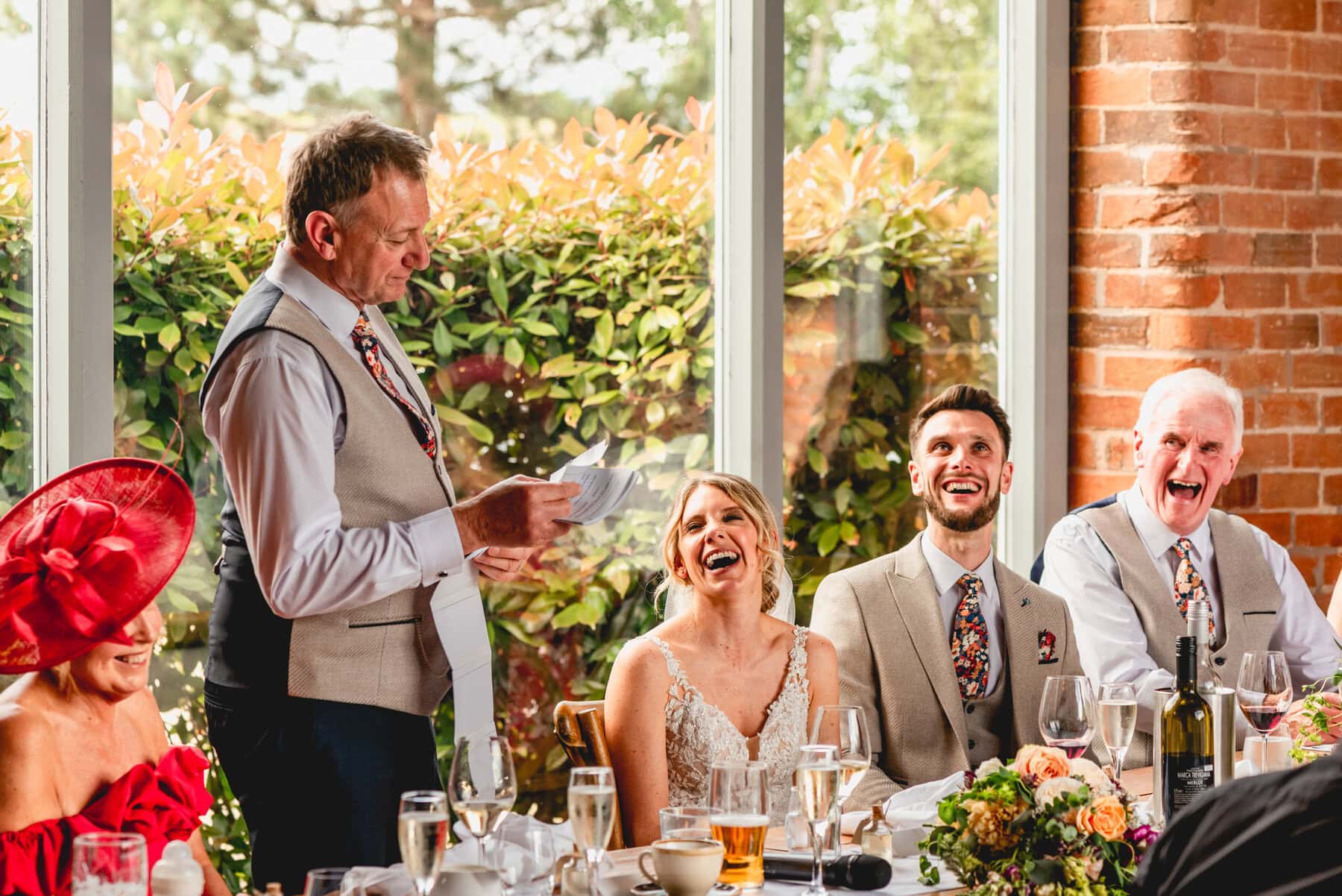 Wedding speeches by father of the bride as bride and groom look on laughing