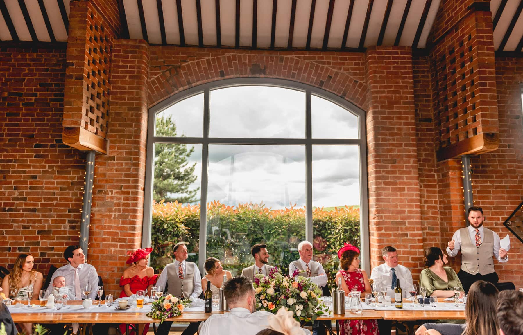 View of top table at a barn wedding venue with large window behind the guests at the top table