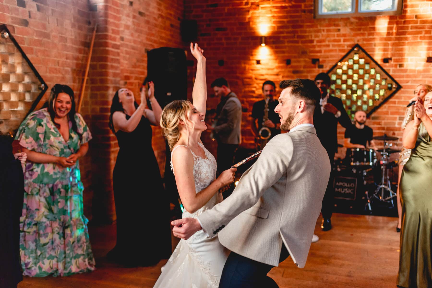Bride and groom dance at their wedding, bride holds groom close by his flowery tie and throws her hand in the air while both sing to the music