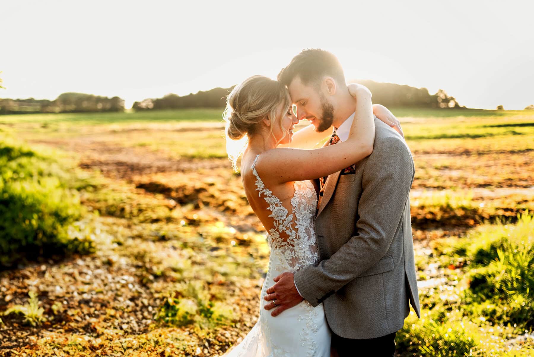 Golden hour photo of bride and groom in a field as the sun sets on their barn wedding