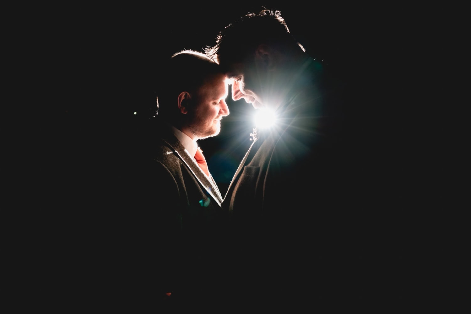 Creative image of two men with heads bowed towards each other on their wedding day - evening portrait. 2025 - A Weird and Wonderful Year of Weddings