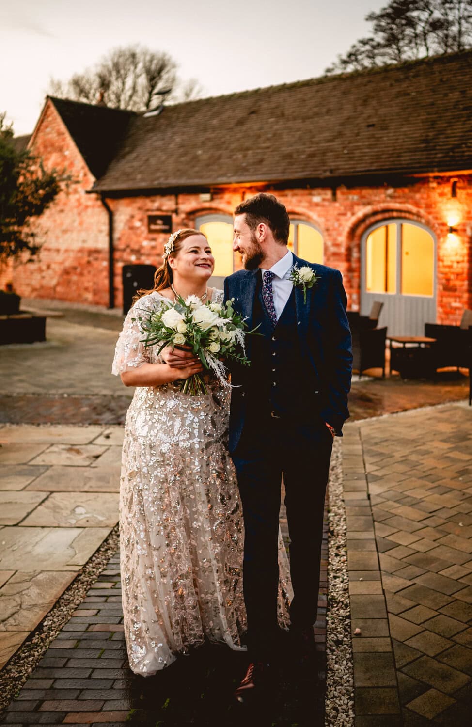 Winter wedding at Christmas at Blackbrook Barns during golden hour, couple walk towards camera looking at each other, bride wears silver embellished dress and holds bouquet