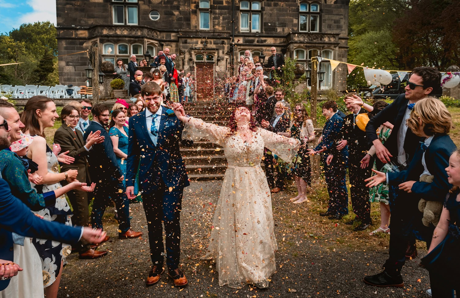 Bride throws hands in the air during confetti toss at Hargate Hall surrounded by a cloud of confetti
